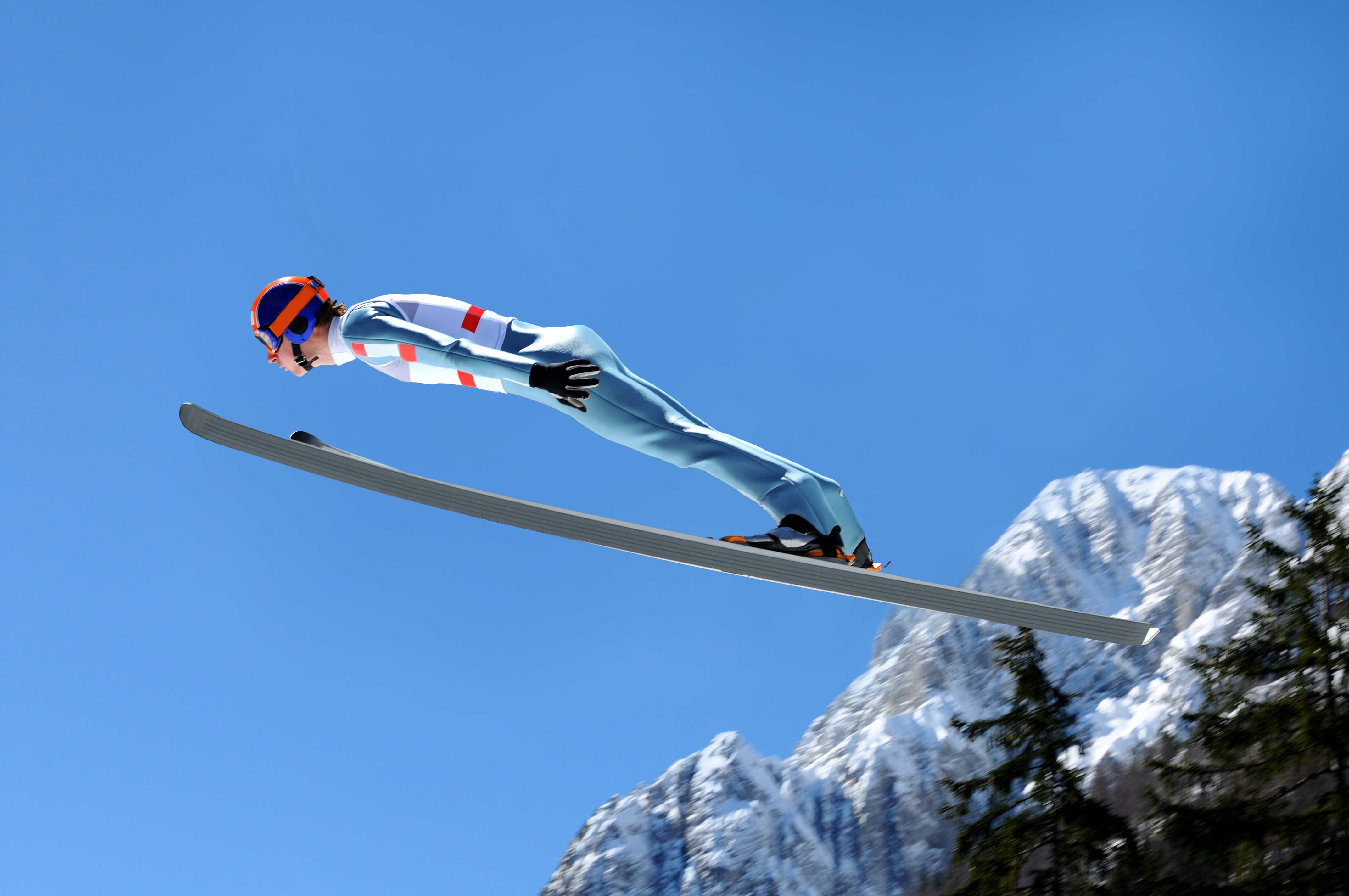Ski jumper flying against the blue sky and the mountain